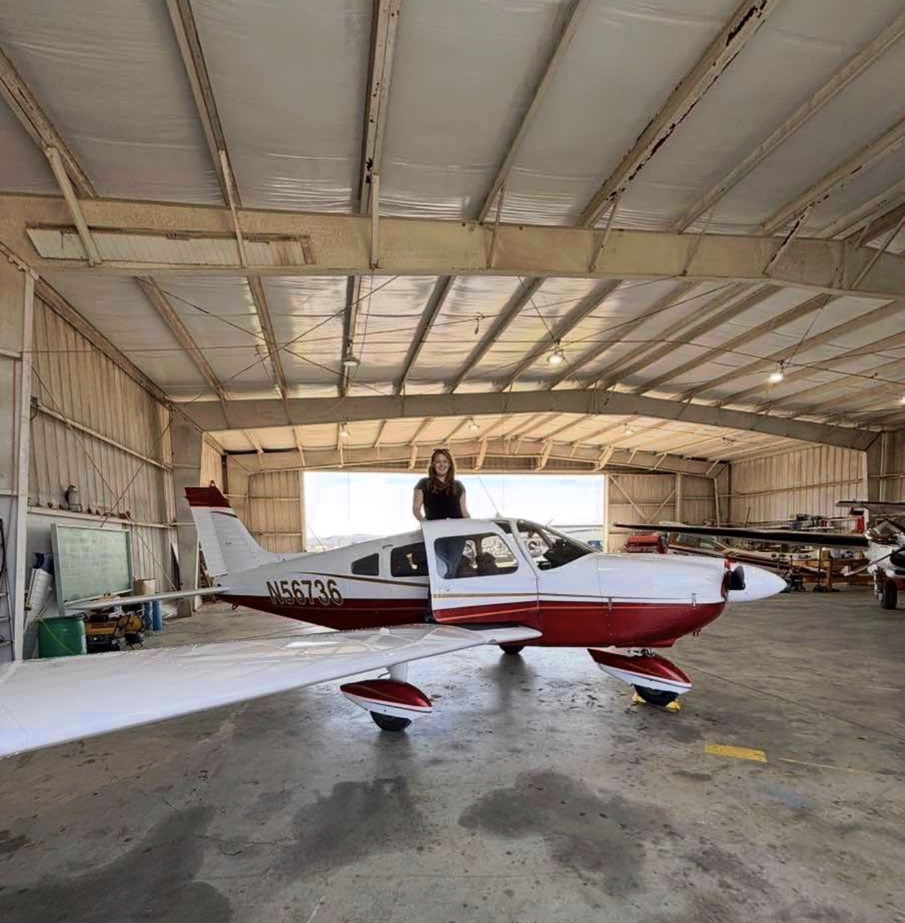 Pilot standing on the wing of a red and white Piper in a hangar